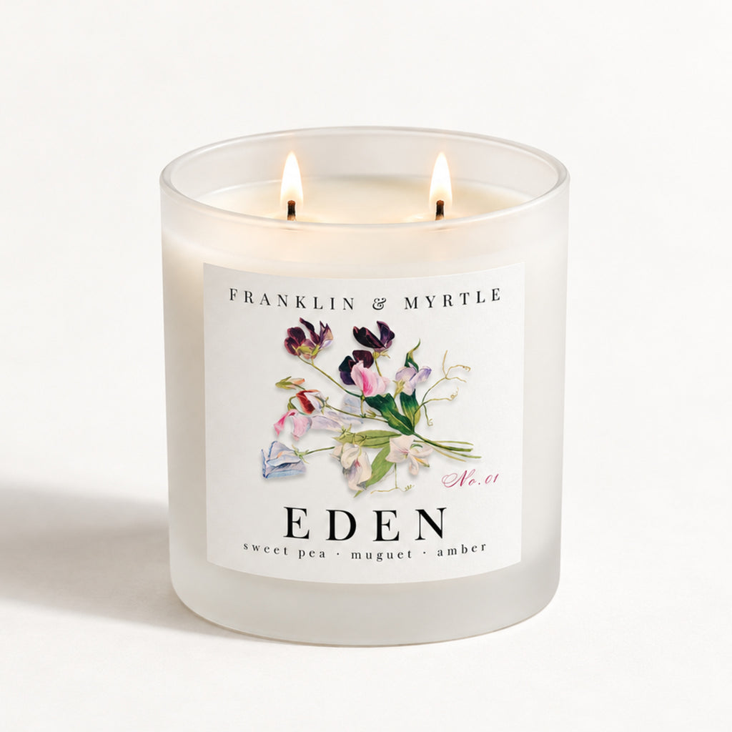 Eden double-wick candle burning in a frosted white glass jar with colorful sweet pea floral label artwork.