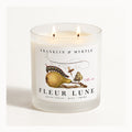 Fleur Lune double-wick candle burning in a frosted white glass jar with pear-and-butterfly label artwork.