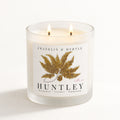 Huntley double-wick candle burning in a frosted white glass jar with golden fern label artwork.