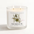 Serein double-wick candle burning in a frosted white glass jar with botanical bird label artwork.