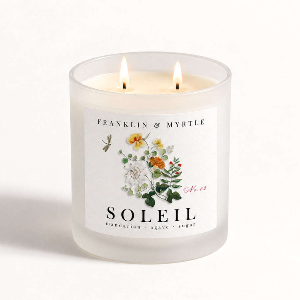 Soleil double-wick candle burning in a frosted white glass jar with colorful botanical label artwork.