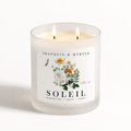 Soleil double-wick candle burning in a frosted white glass jar with colorful botanical label artwork.