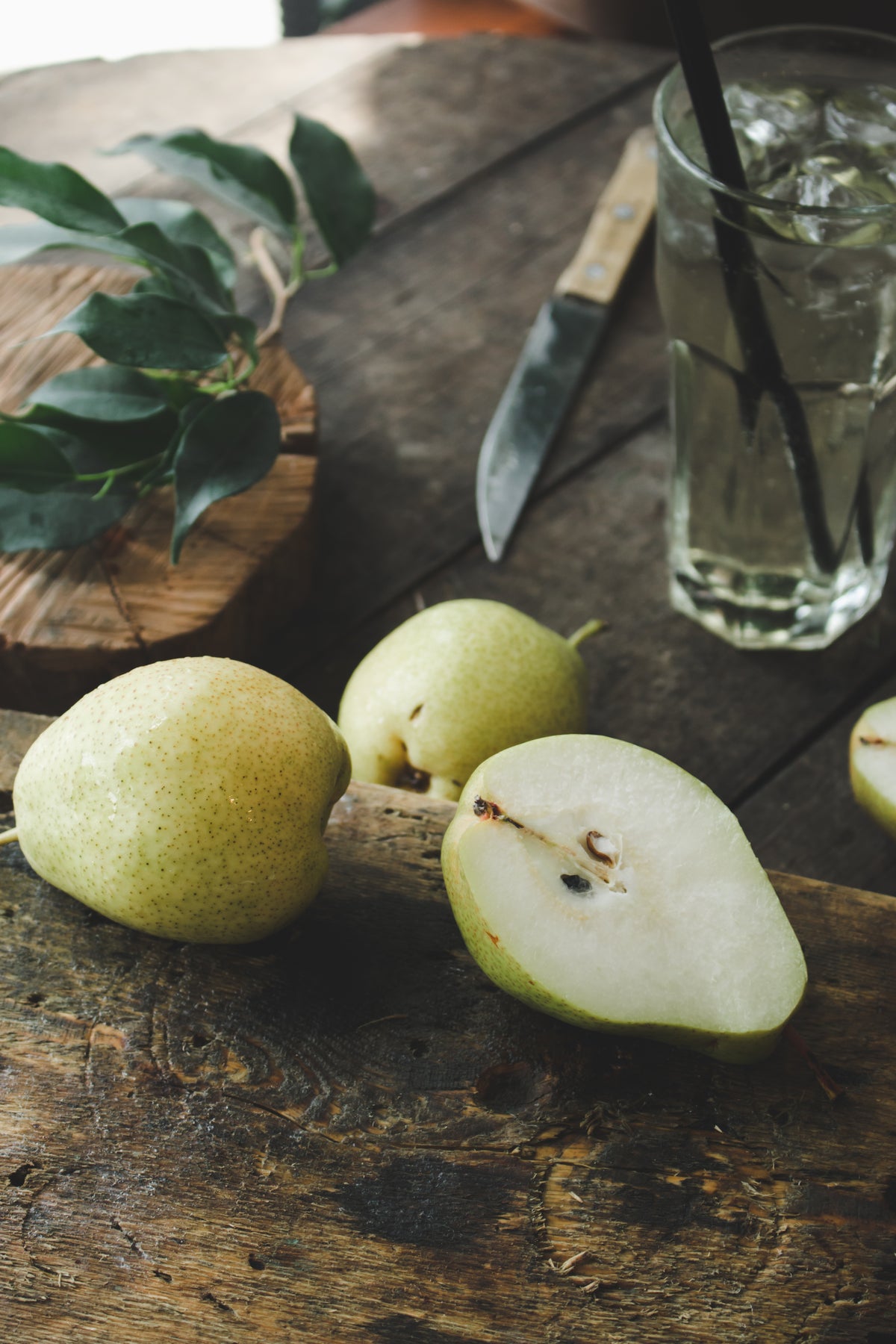 Whole and sliced green pears on a dark wooden table, representing the pear fragrance note in Fleur Lune.