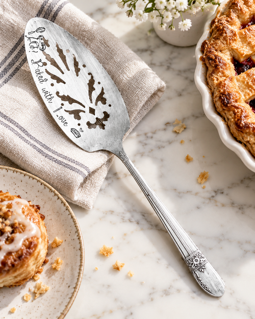 Vintage silver pie server engraved “Baked with Love” styled with pastries on a marble countertop.