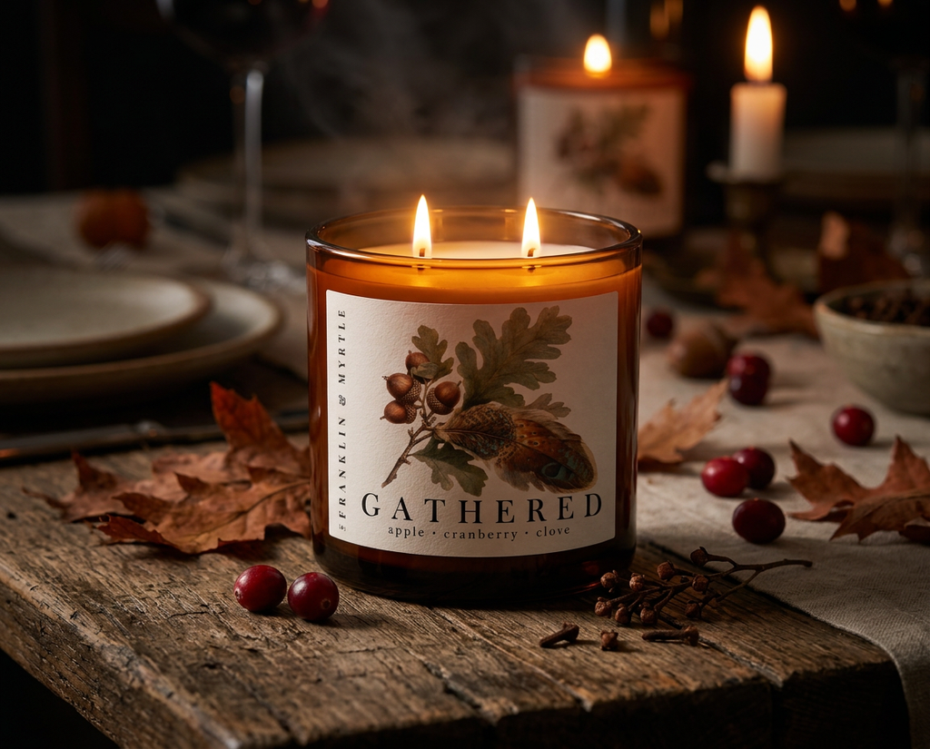 Lit Gathered candle in an amber glass jar on a rustic table with cranberries, cloves, and fallen leaves scattered around it.