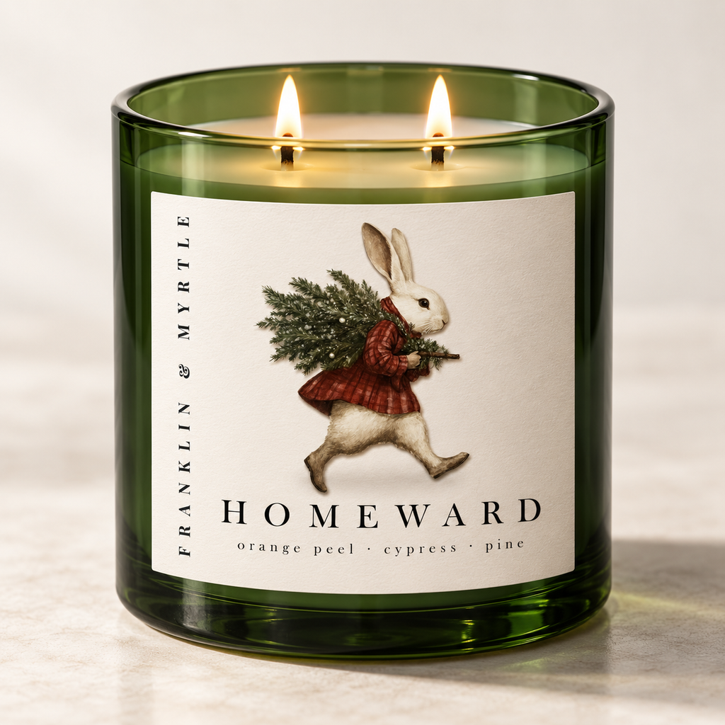Lit Homeward candle in a dark green glass jar with two wicks and a label showing a rabbit carrying pine branches