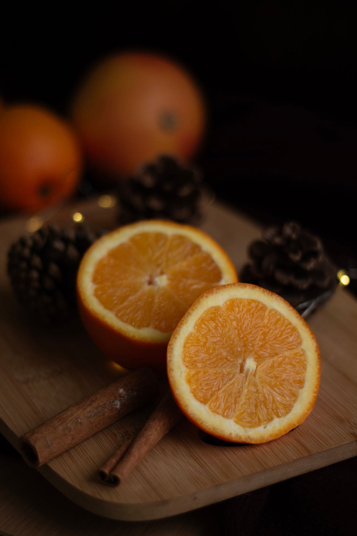 Halved oranges and cinnamon sticks on a wooden board with pinecones nearby