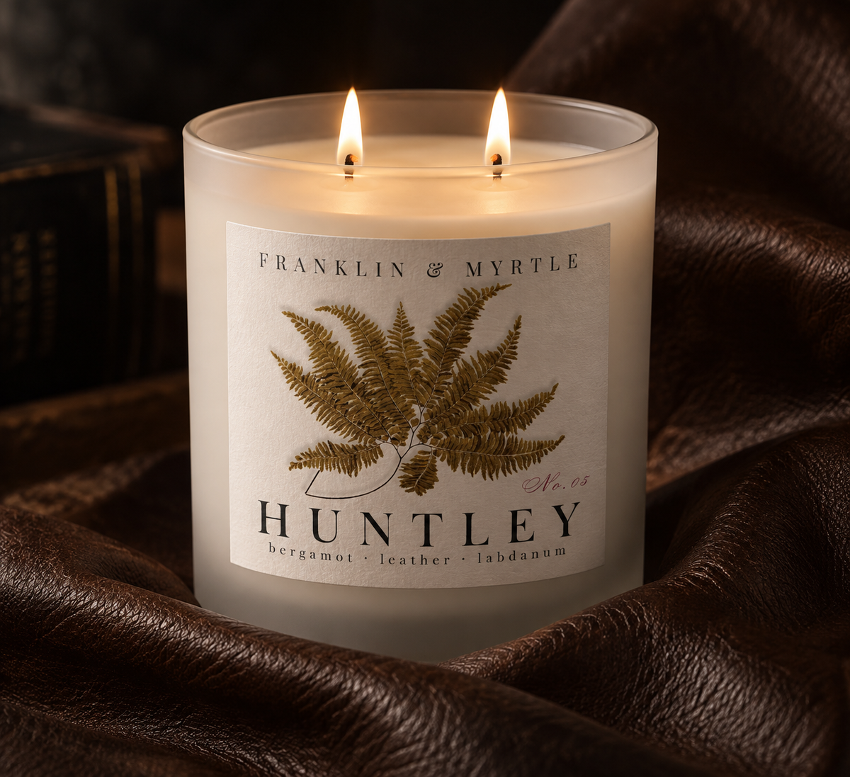 Lit Huntley double-wick candle in frosted white glass nestled in dark brown leather.