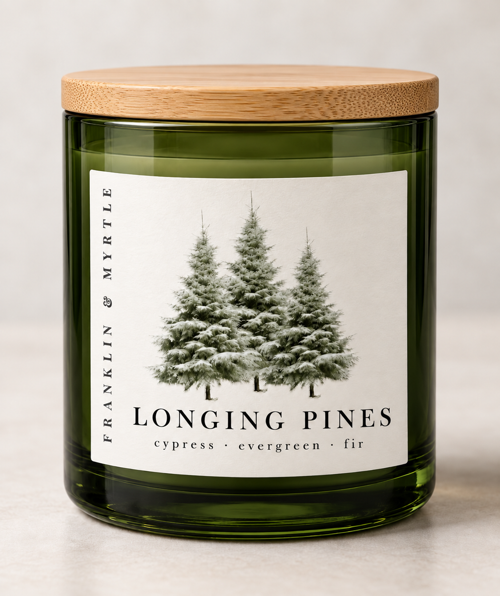 Longing Pines candle in a dark green glass jar with a bamboo lid and a pine tree label against a light background.