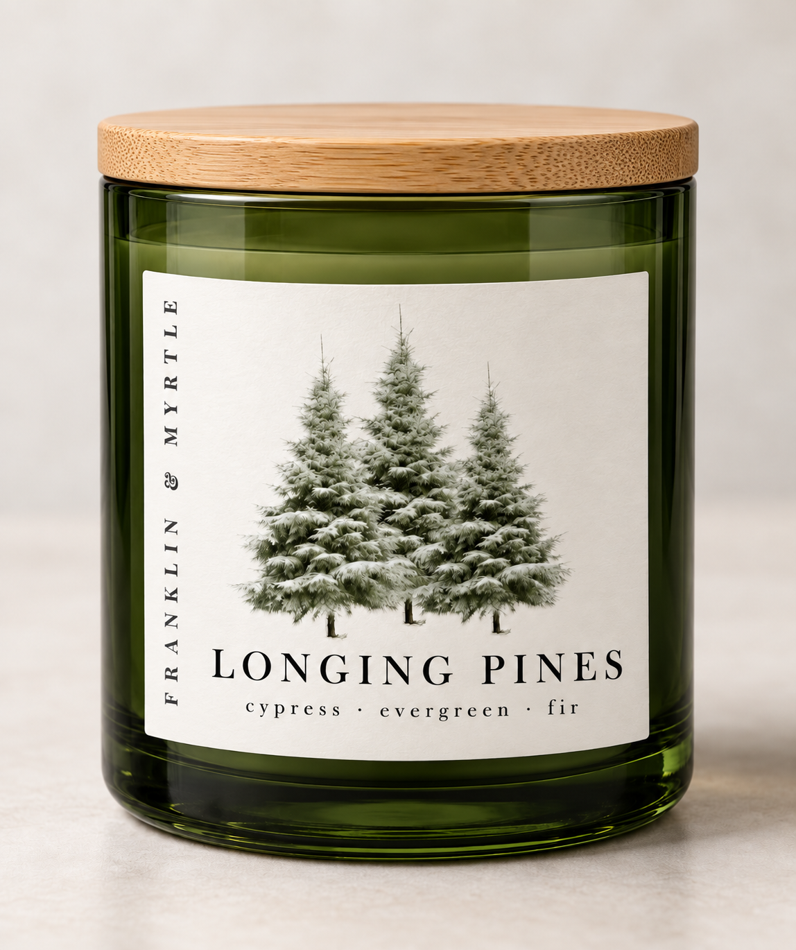 Longing Pines candle in a dark green glass jar with a bamboo lid and a pine tree label against a light background.