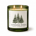 Longing Pines candle in a dark green glass jar with two lit wicks and a pine tree label against a light background.