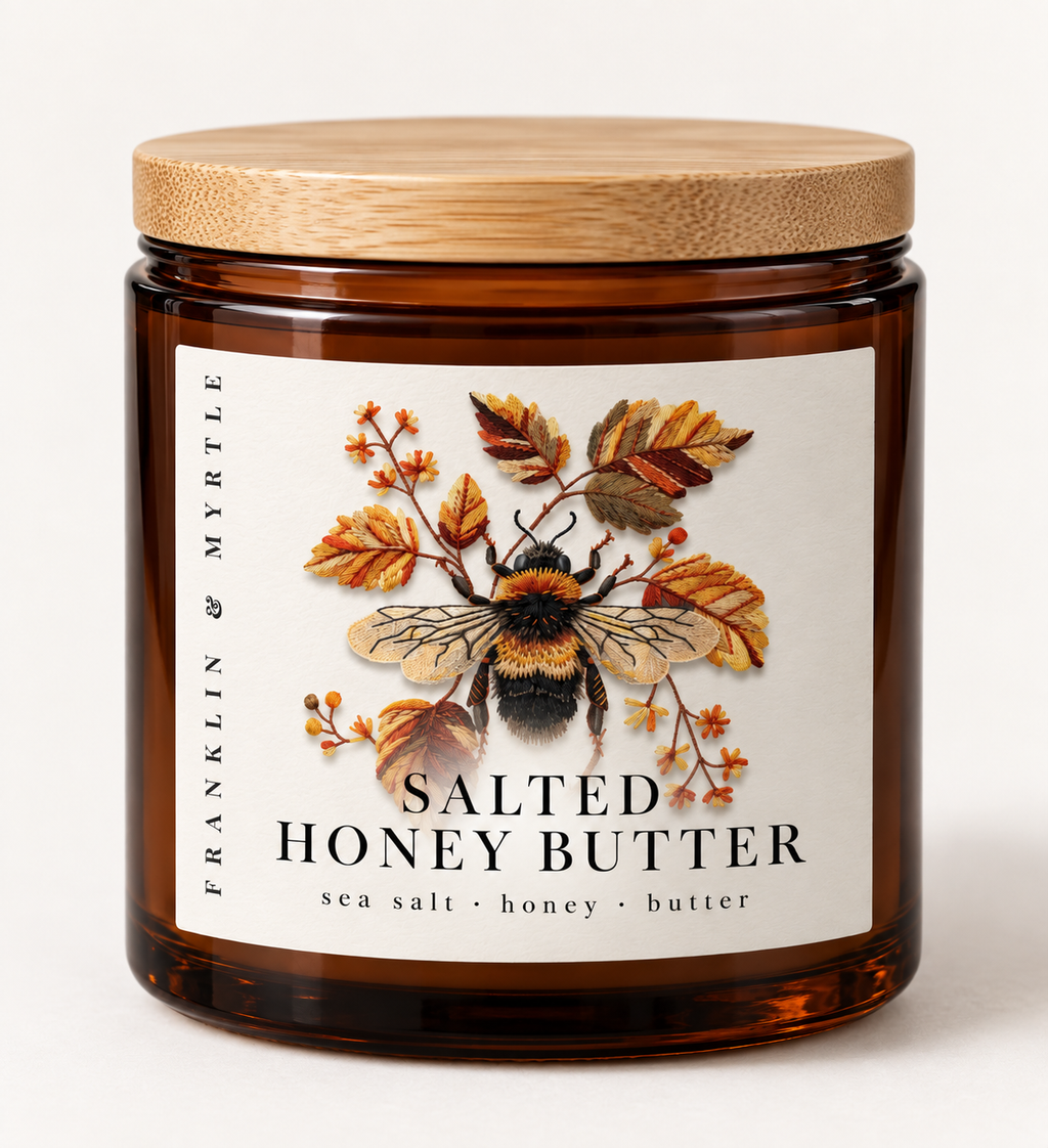 Salted Honey Butter candle in an amber glass jar with a bamboo lid and a label showing a bumblebee among autumn leaves