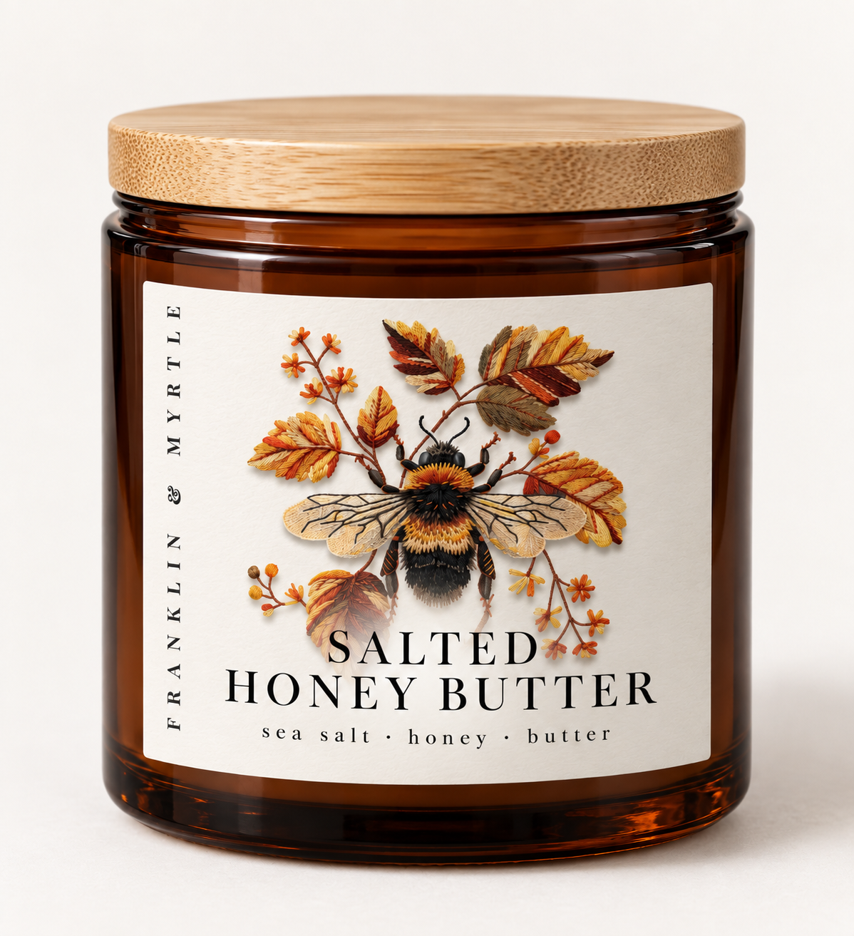 Salted Honey Butter candle in an amber glass jar with a bamboo lid and a label showing a bumblebee among autumn leaves
