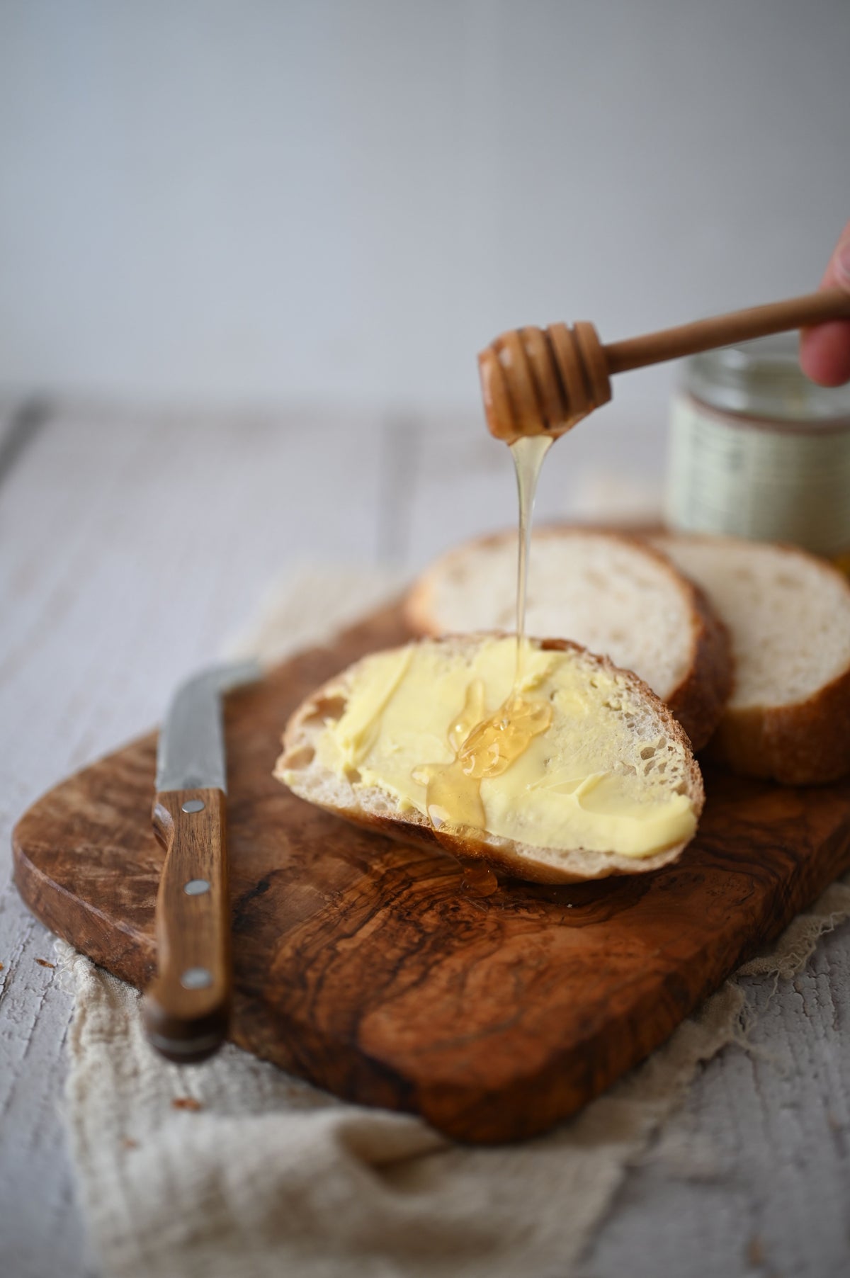 Honey drizzled from a wooden dipper onto a slice of buttered bread on a cutting board.
