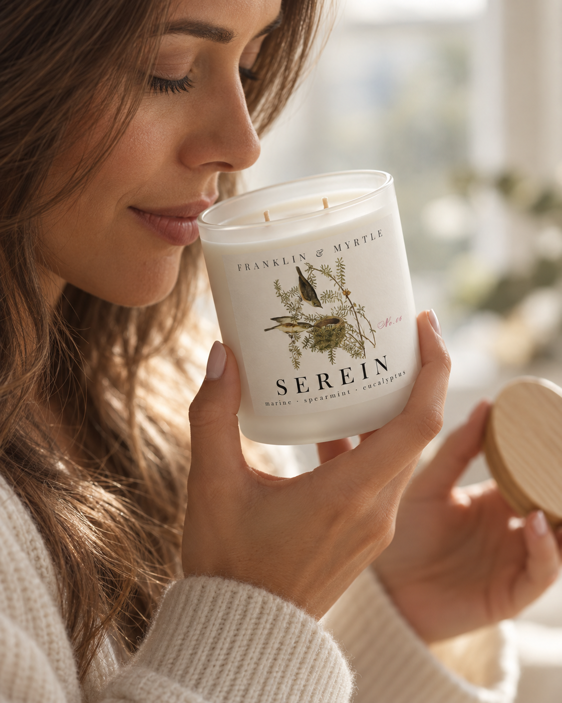 Woman smelling an unlit Serein candle in a frosted white glass jar while holding its bamboo lid.