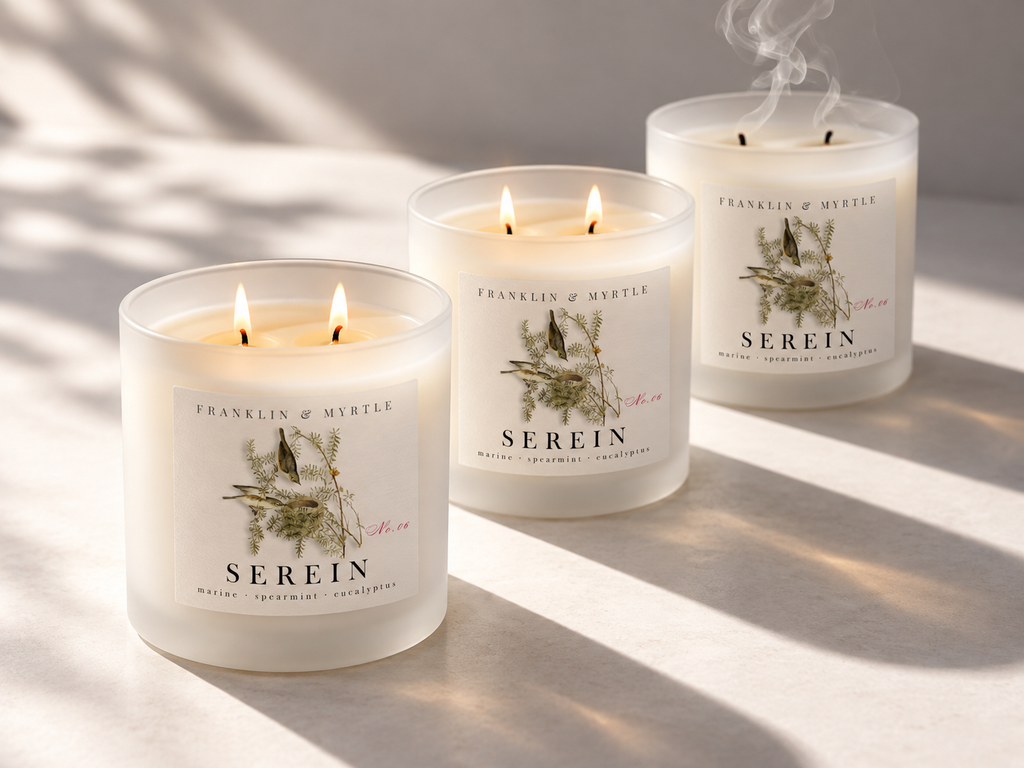 Three frosted white Serein candles in warm sunlight; two are burning and one has just been extinguished.