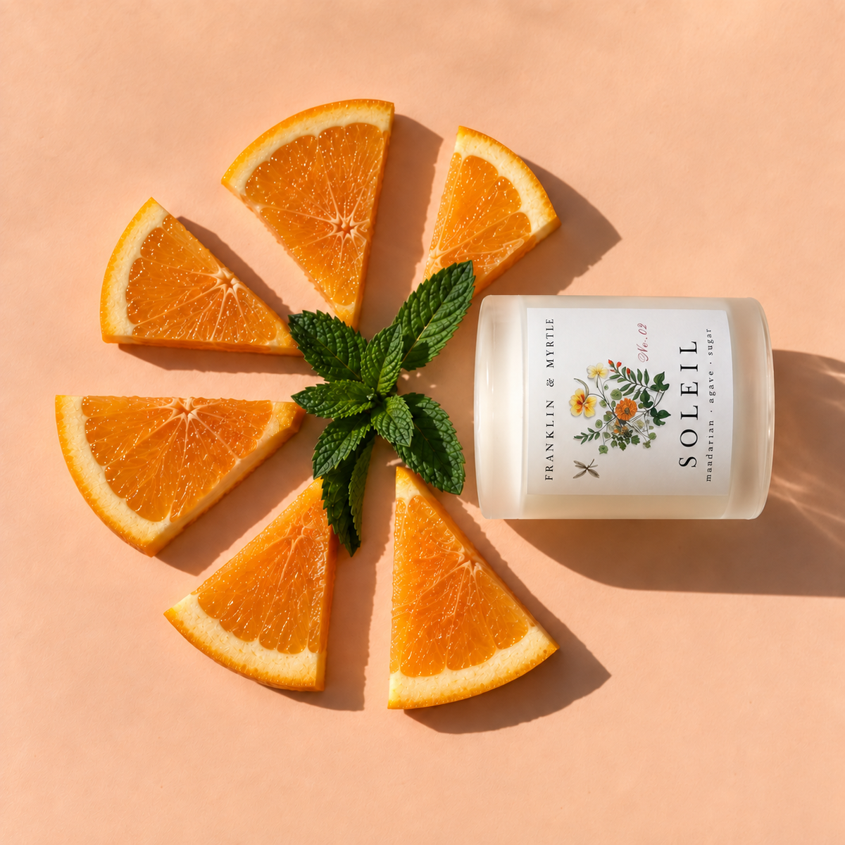 Frosted white Soleil candle jar lying on its side among sliced oranges and fresh mint.