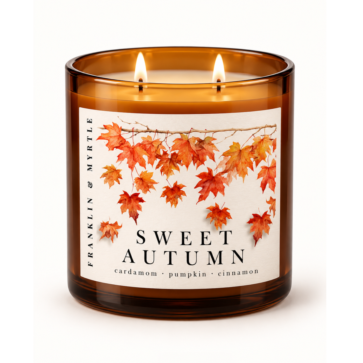 Lit Sweet Autumn candle with two flames in an amber glass jar.  The label features falling orange and red leaves above the note cardamon, pumpkin, and cinnamon