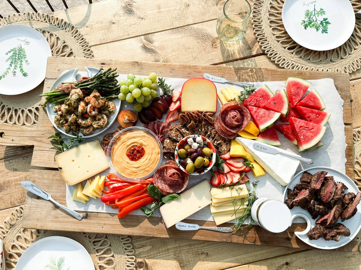 Vintage hand-stamped silver-plated spreaders styled on a large charcuterie board with cheese, fruit, meats, and vegetables.