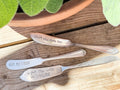 Three hand-stamped vintage silver-plated charcuterie spreaders arranged on a wooden surface.