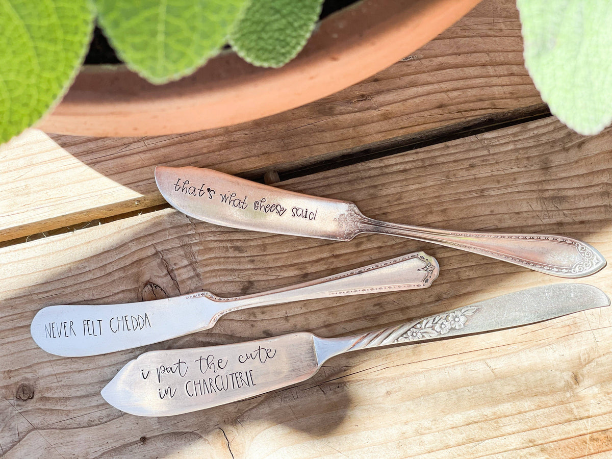Three hand-stamped vintage silver-plated charcuterie spreaders arranged on a wooden surface.