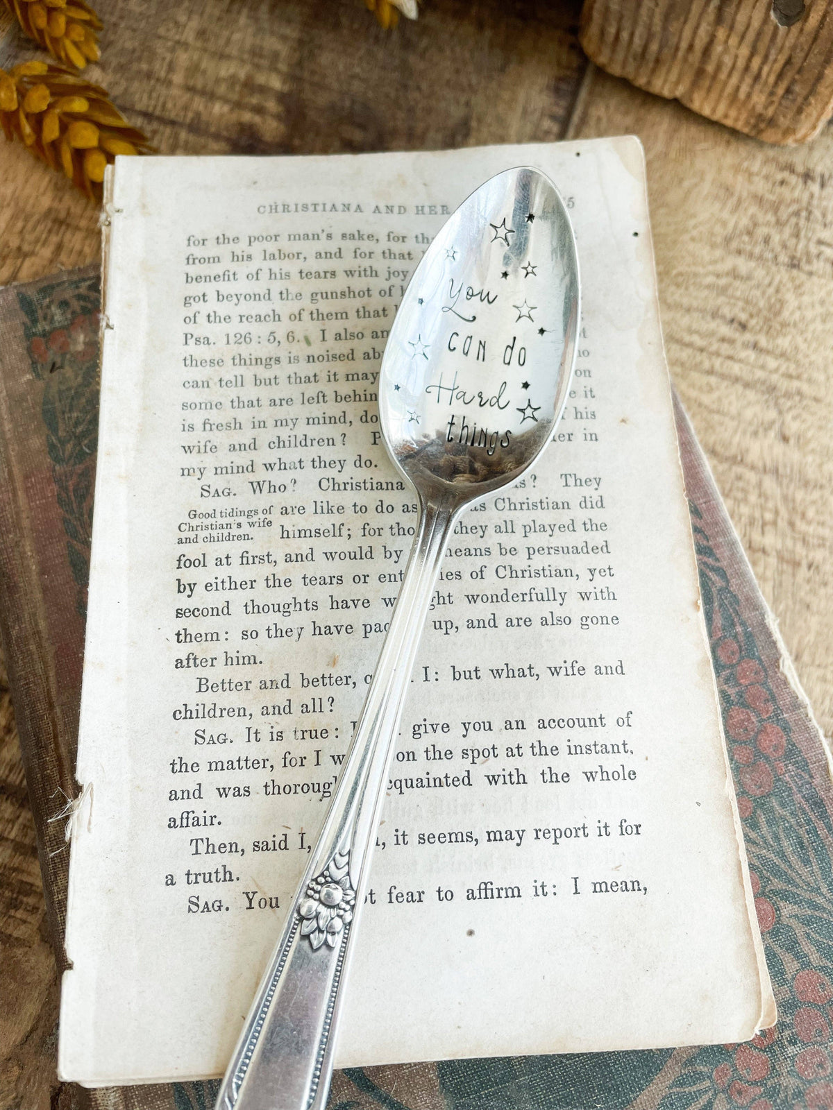 Vintage silver spoon stamped “You Can Do Hard Things” with star details, styled on the pages of an old book.